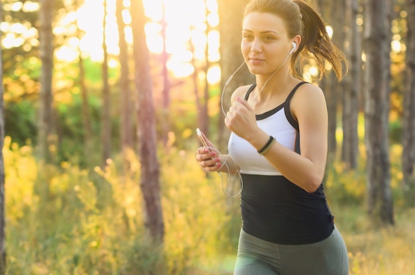 Frau mit Fitness Armband und Kopfhörern beim Jogging im Wald